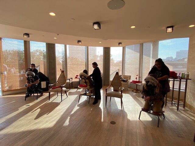 A professional indoor wellness space featuring multiple massage therapists providing seated chair massages to clients near large windows.