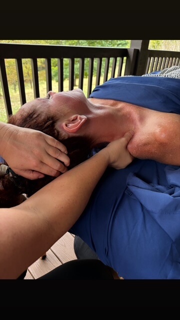A close-up view of a licensed massage therapist performing a therapeutic neck and shoulder release on a client on an outdoor deck.